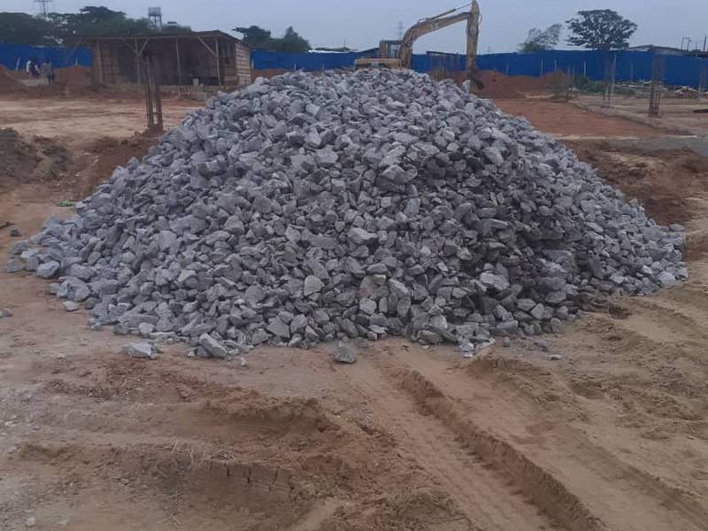 Pile of granite delivered to a building site with an excavator behind